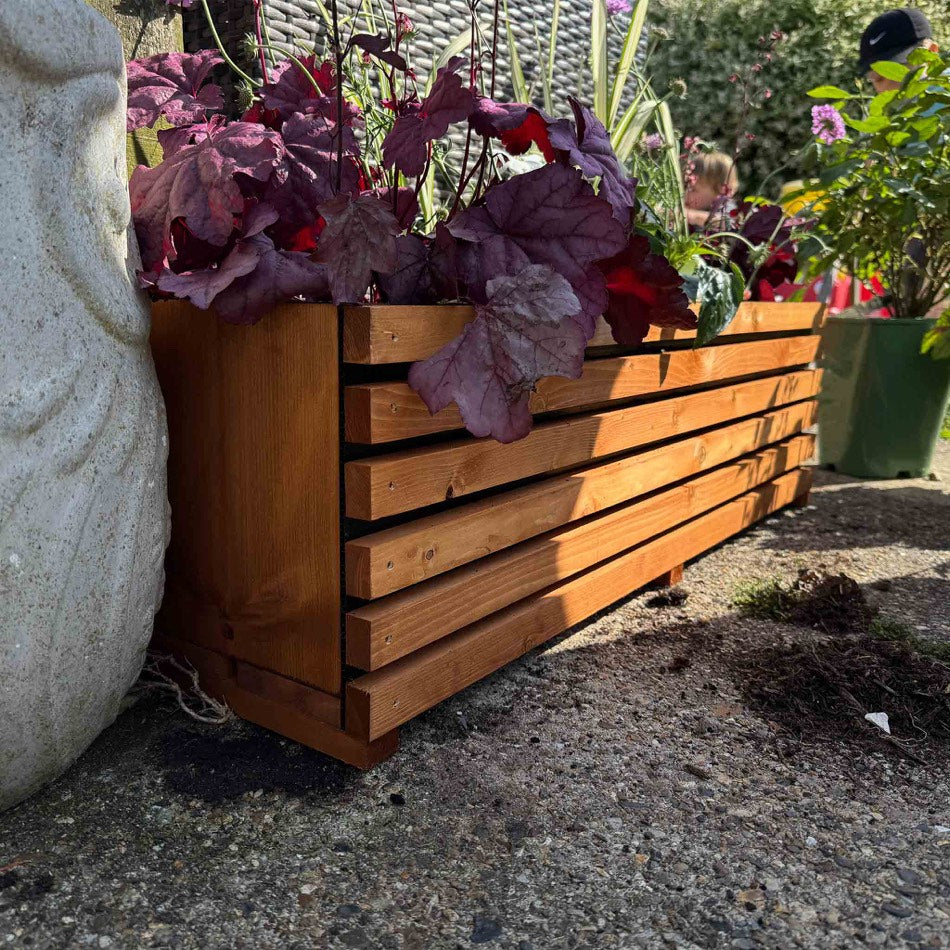 The 2ft tan Sussex planter, slatted timber sides on a raised base, planted and standing in a garden